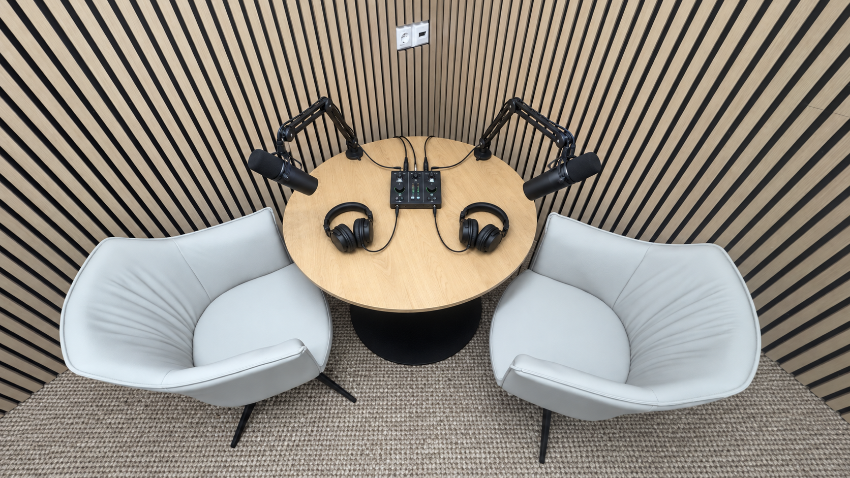 Two-seater podcast table with microphones, headphones and audio interface against wood slat wall